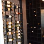 We used a single-deep, wall-mounted metal wine rack for this Orange County glass wine cellar and installed them on the sides of the cellar. This way, we were able to utilize the extra space without obstructing the central wooden wine shelves.